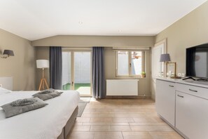 A modern hotel room with a bed, a desk, a television, and a view of a green outdoor area. - Inn Bruges Suites (Bruges)