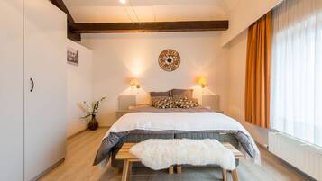 Een slaapkamer met een bed, bedlampen, een klok, een raam met gordijnen, en een houten bankje.