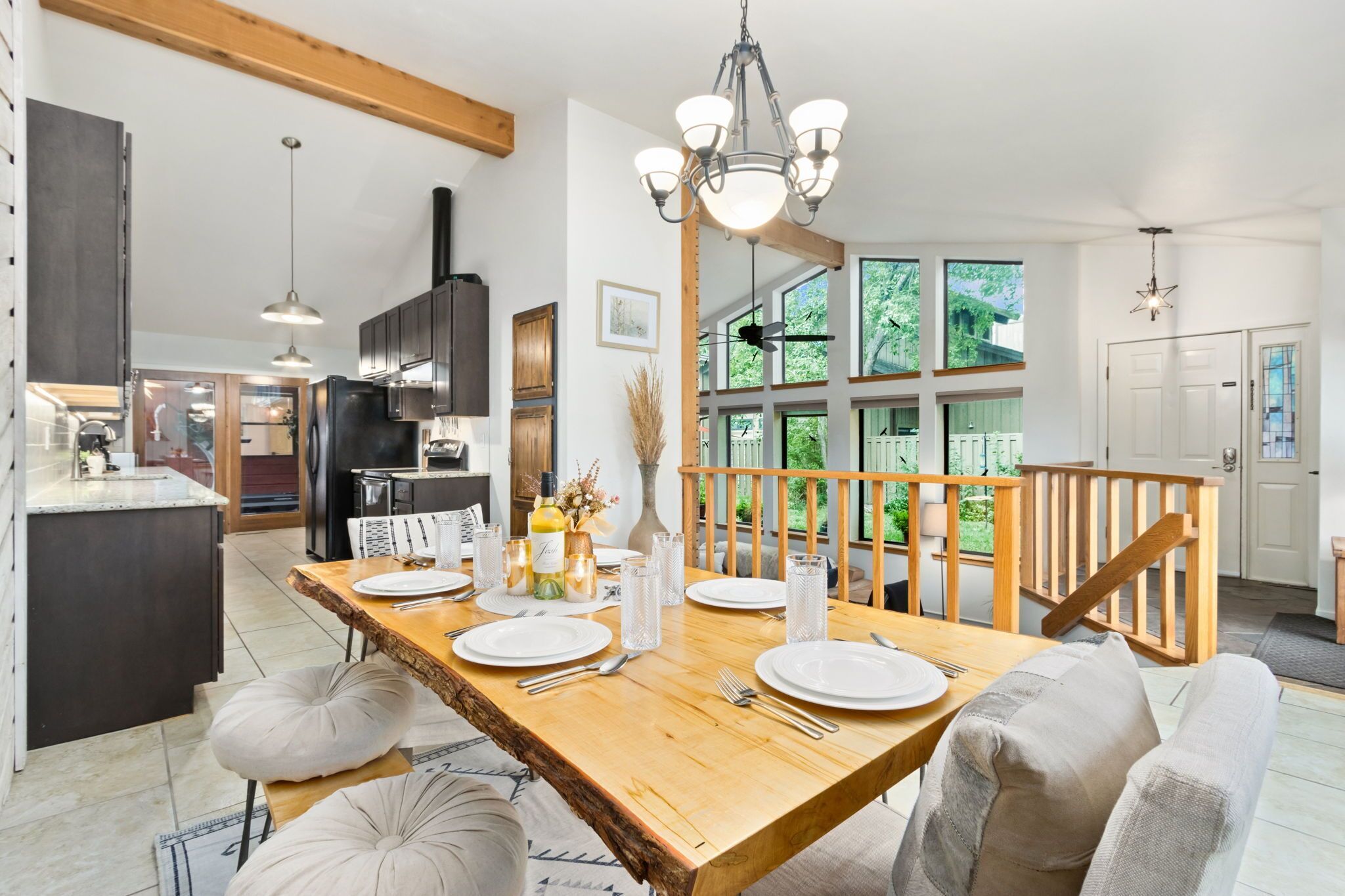 A modern kitchen with dark cabinets, a wooden dining table set for four, and a view of the outdoors through large windows.