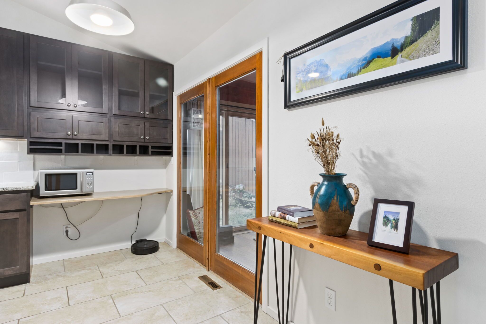 A modern kitchen with dark cabinets, a microwave, and a robotic vacuum cleaner.