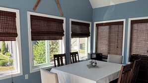 A dining room with a large table, four chairs, and a bench. There are four windows with brown blinds, and a wooden cross is mounted on the wall above the windows. - Fabulous 3-bedroom Weirs Beach Village home in Laconia. (Laconia)