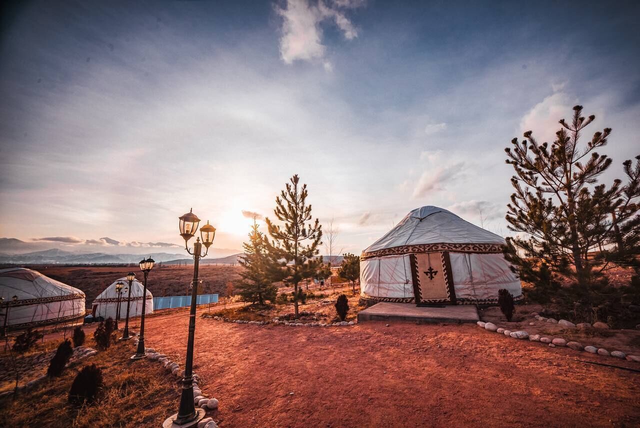 A yurt with a patterned entrance, surrounded by trees and a dirt path.
