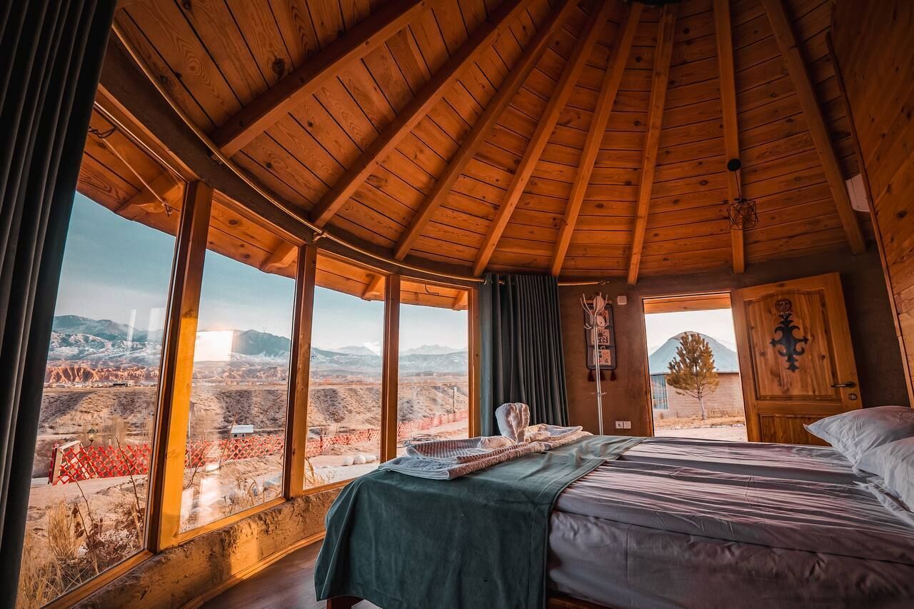 A wooden room with a bed, large windows, and a view of a mountainous landscape.
