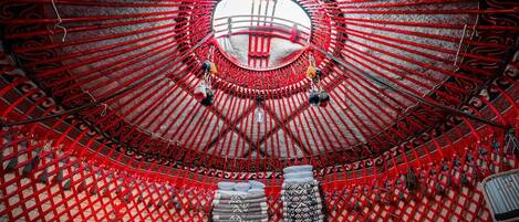 A traditional yurt with a circular entrance, red lattice walls, and patterned cushions.