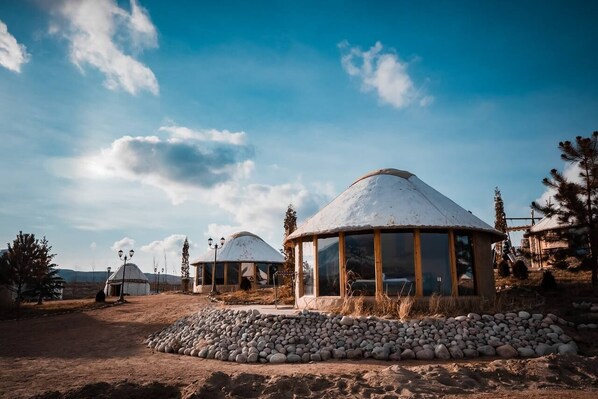 A yurt with a snow-covered roof, a stone wall in front, and a clear blue sky in the background.