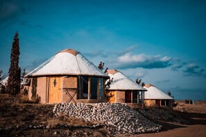 A series of traditional yurts with conical roofs, arranged in a row on a hillside.