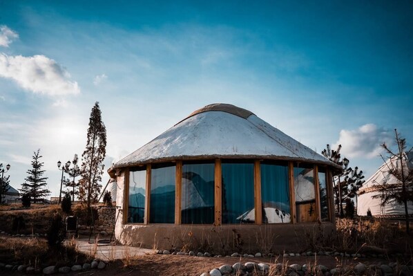 Una yurta tradicional con techo cónico, ventanas amplias y base de piedra.