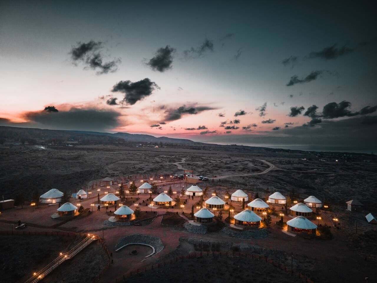 A yurt settlement with multiple yurts arranged in a circular pattern, connected by pathways, and illuminated by artificial lights.