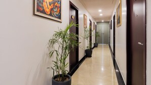 Un pasillo de hotel con puertas, obras de arte enmarcadas y plantas en macetas.