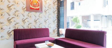 A modern interior with two maroon sofas, a white coffee table, and a floral wallpaper.