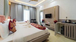 A modern hotel room with a large bed, a desk with a flat-screen TV, a ceiling fan, and a minibar. - Hotel RD Ganpati Palace (Danta Ramgarh)