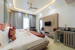 A modern hotel room with a large bed, a desk with a flat-screen TV, a ceiling fan, and a minibar. - Hotel RD Ganpati Palace (Danta Ramgarh)