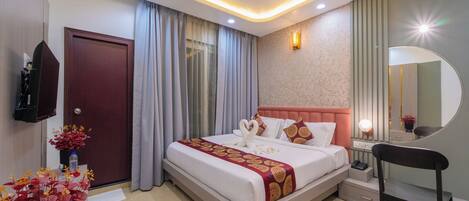 A modern hotel room with a large bed, a ceiling fan, a bedside table, a chair, and a mirror.