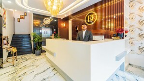 Zona de recepción de hotel con diseño moderno, que incluye un mostrador de recepción, una araña y una escalera, además de un cartel que dice 'Se reserva el derecho de admisión'.