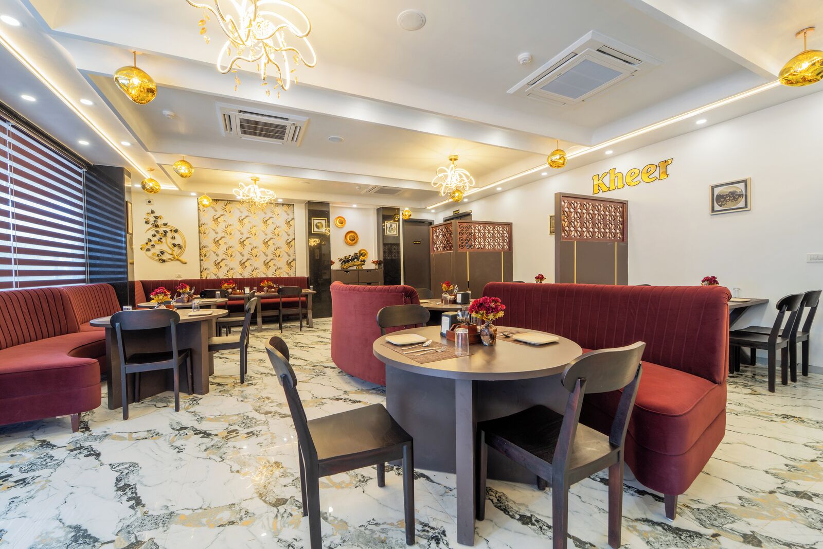 Un restaurante con asientos tapizados en rojo, mesas redondas y candelabros modernos.