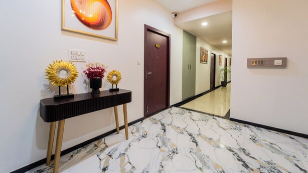 A hallway with a marble floor, a console table with decorative flowers, a framed abstract painting, and a door at the end. - Hotel RD Ganpati Palace (Danta Ramgarh)