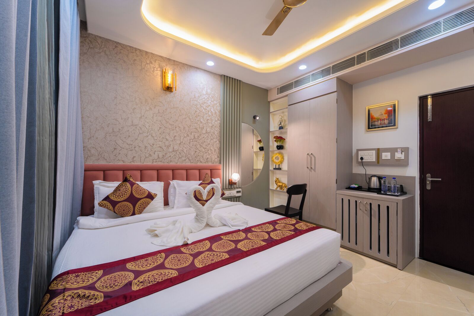 A modern hotel room with a large bed, a vanity with a mirror, and a desk with a chair.