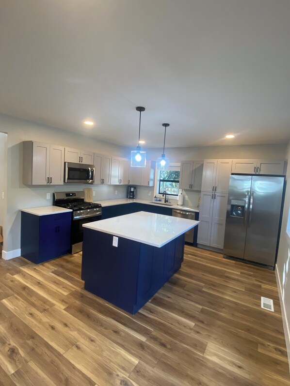A modern kitchen with white cabinets, a stainless steel refrigerator, a central island, and wooden flooring.