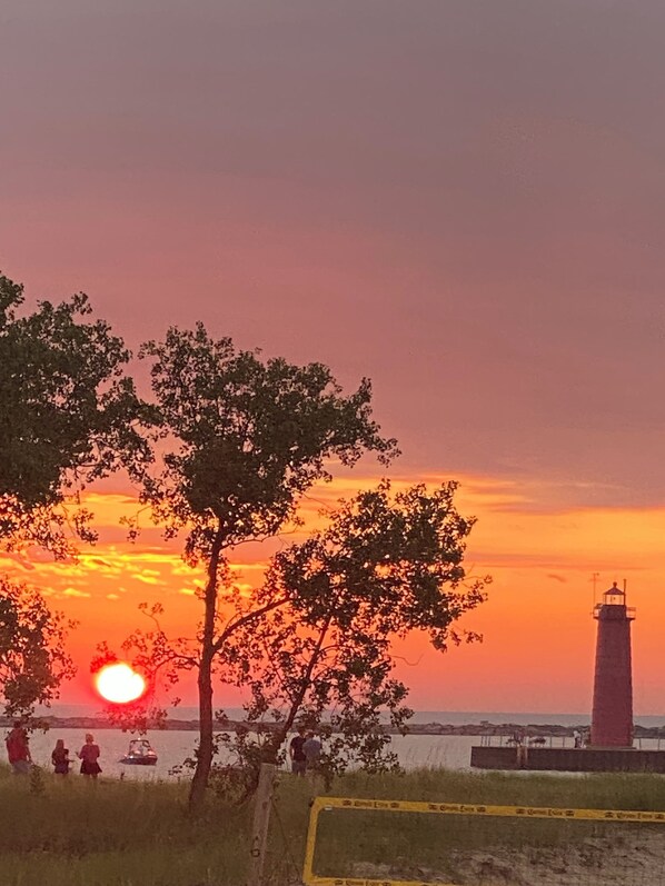 Vista do pôr do sol com um farol e pessoas em primeiro plano.