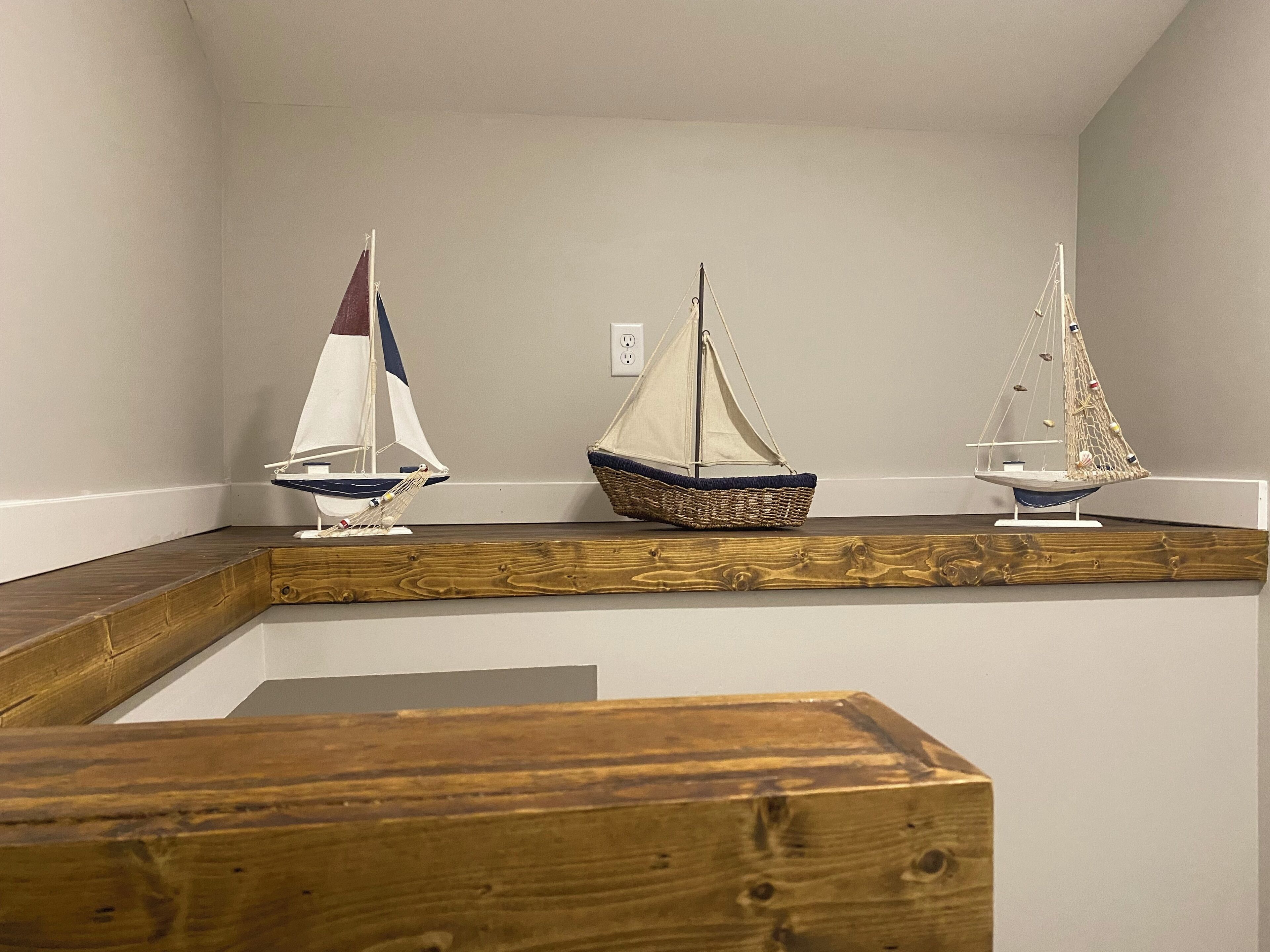 Three model sailboats on a wooden shelf against a plain wall.