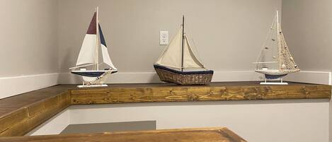Three model sailboats on a wooden shelf against a plain wall.