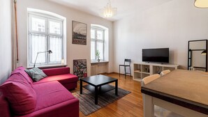 A living room with a red sofa, a black coffee table, a TV, and a dining area with a table and chairs. - RentPlanet - Apartament Kotlarska II (Wrocław)