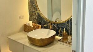 A bathroom with a marble backsplash, a round mirror, a white sink, and a stone pathway leading to the door. - Ocean View Apartment in Condado (San Juan)