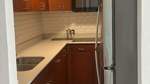 A compact kitchen with wooden cabinets, a stainless steel refrigerator, and a microwave. - Ocean View Apartment in Condado (San Juan)