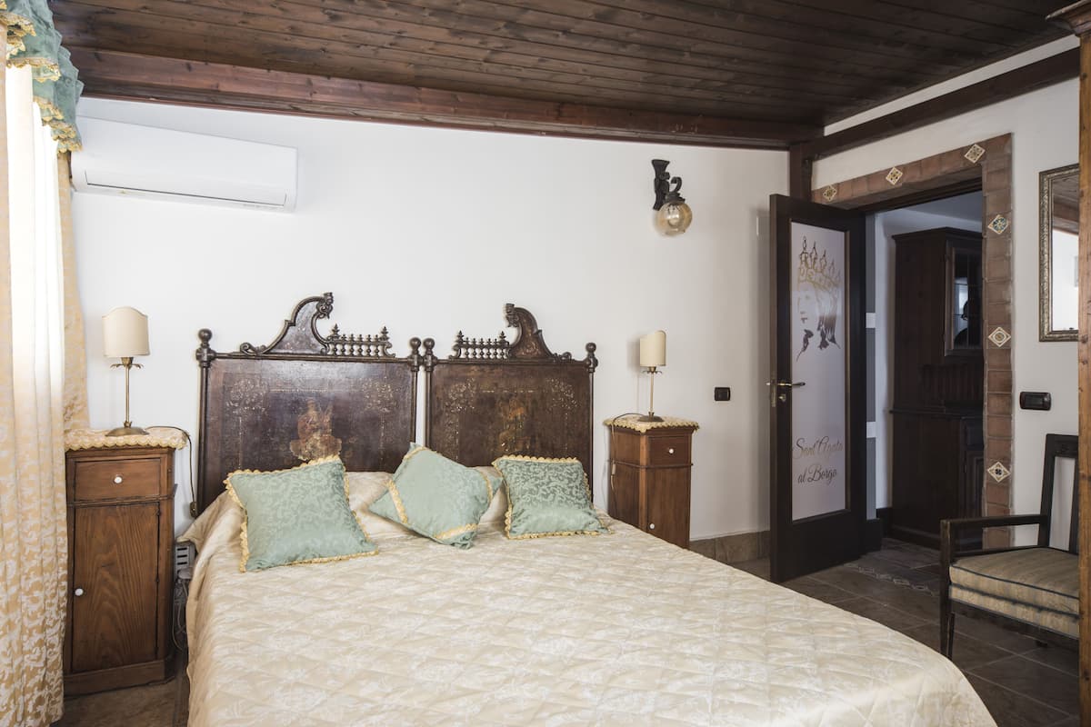 A bedroom with a large bed, two nightstands, a wooden headboard, a wall-mounted light fixture, and a door with a decorative frame.
