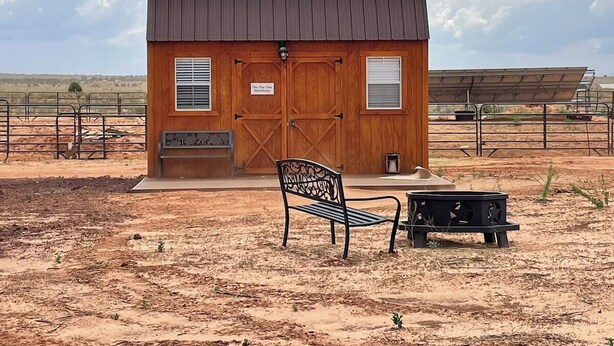 Un pequeño edificio de madera con techo metálico, una banca y una mesa al frente.