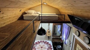 Un interior de madera acogedor con una litera, una lámpara colgante, una guitarra y una pequeña cocina.