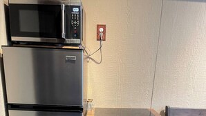 Una cocina compacta con refrigerador de acero inoxidable, microondas y encimera de madera con cajones.