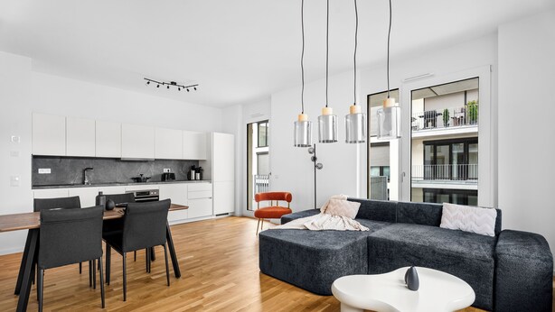 Una sala moderna con un sofá seccional gris, una mesa de centro blanca y un comedor con una mesa de madera y sillas negras.