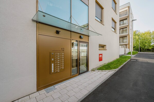 Un edificio moderno con entrada de vidrio, puerta numerada y un pequeño jardín.