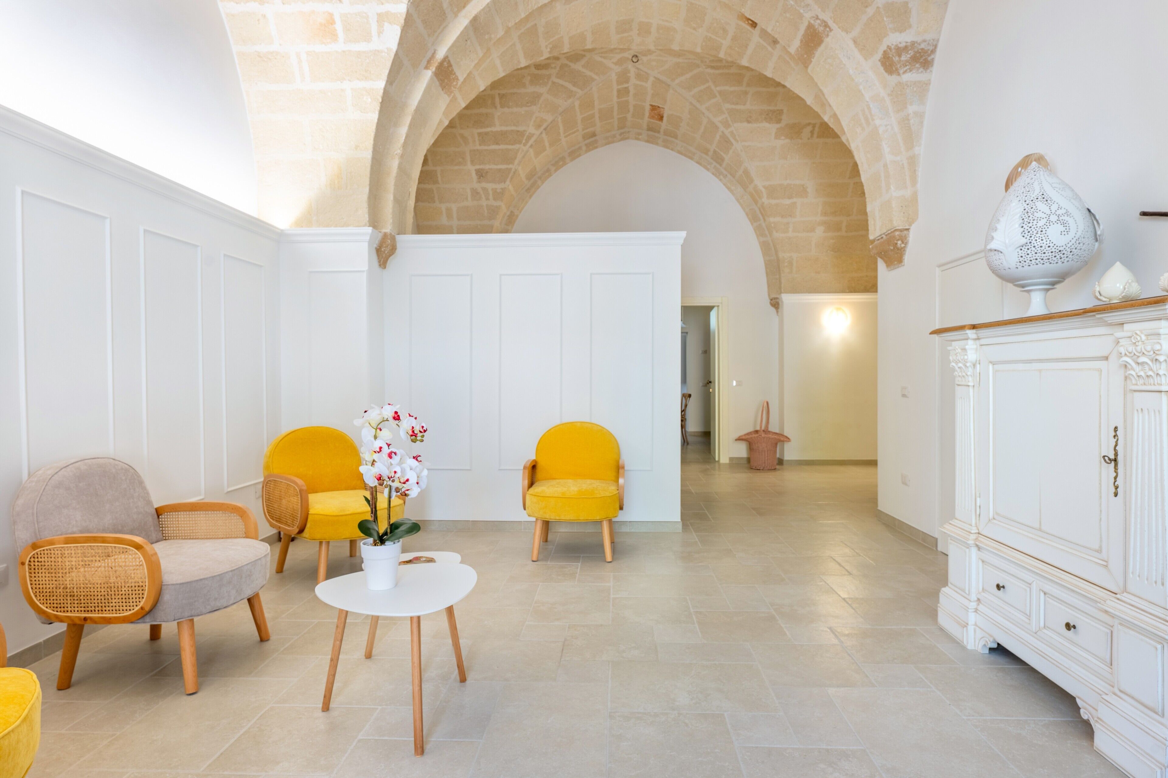 A room with a white door, yellow chairs, a white table with a vase of flowers, and a white cabinet.