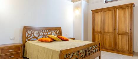 A bedroom with a wooden bed, a nightstand, a wardrobe, and a small window.