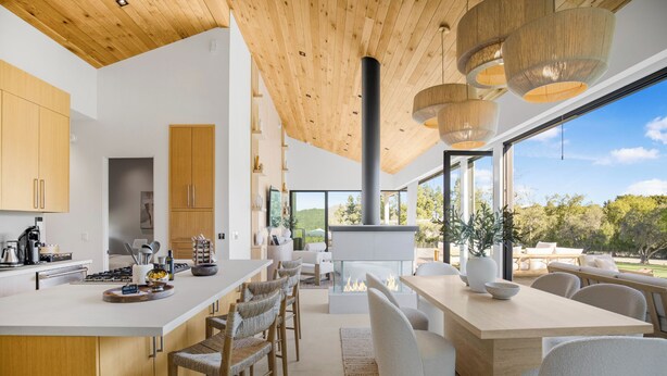 Eine moderne Küche mit einer großen Kochinsel, Holzboden und großen Fenstern mit Blick ins Freie.
