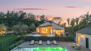 Ein modernes Haus mit Pool, Sitzgelegenheiten im Freien und Blick auf den Sonnenuntergang.