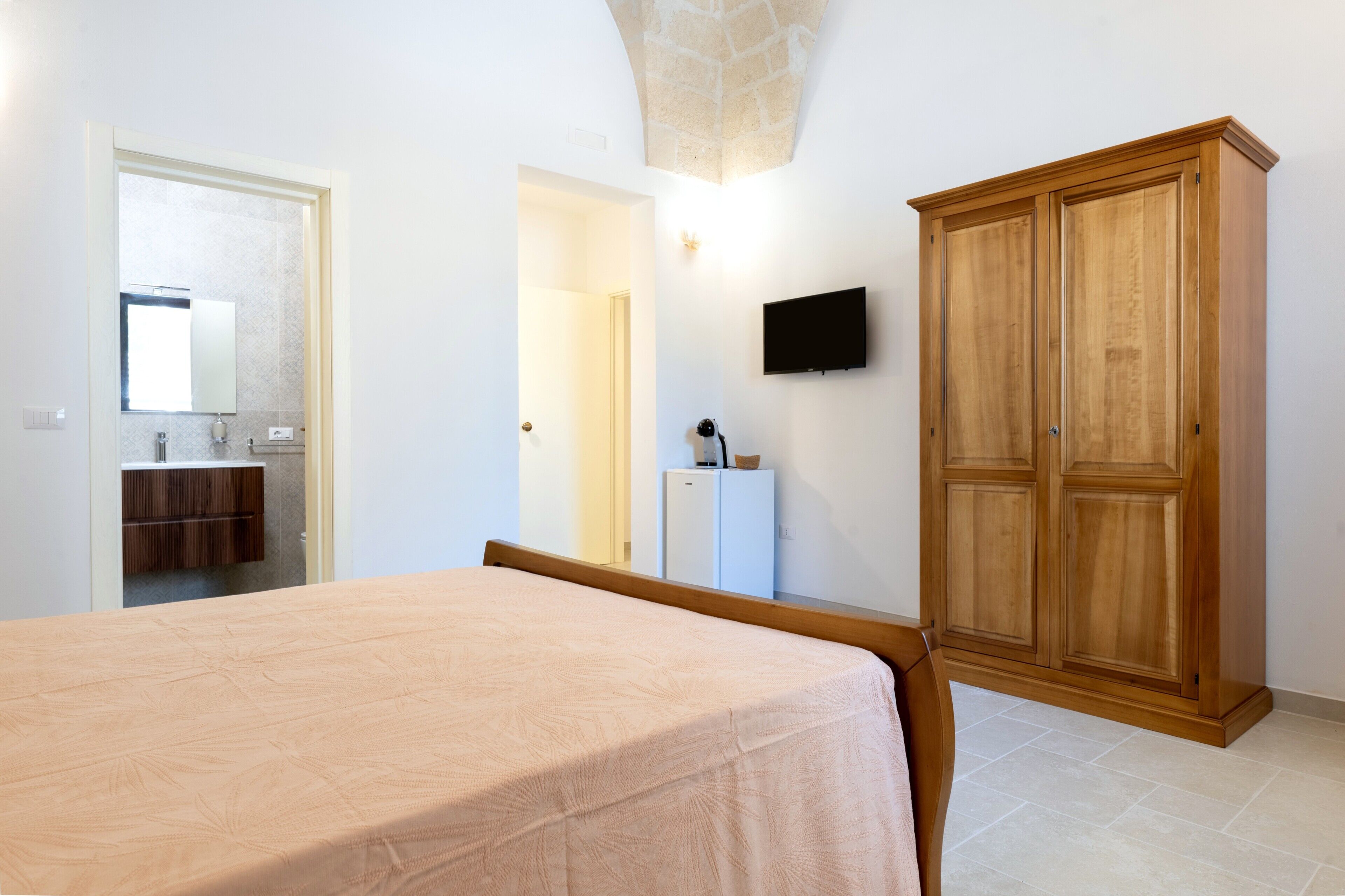 Una camera da letto con un letto, un armadio, una televisione e un bagno visibile attraverso una porta aperta.