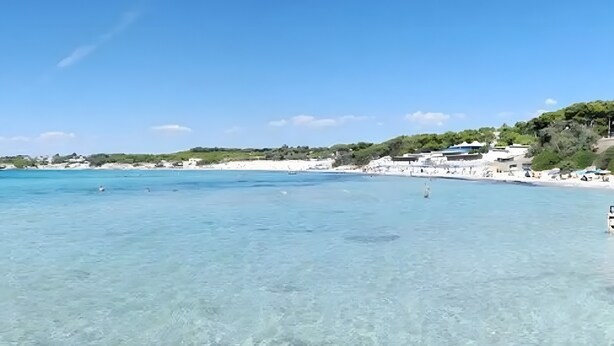 A coastal scene with clear turquoise water, a sandy beach, and buildings in the background. - Room 'Piano Terra' with Private Garden, Wi-Fi and Air Conditioning (Pulsano)