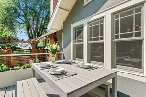 Un área de comedor al aire libre con una mesa lista para cuatro personas, rodeada de amplios ventanales.