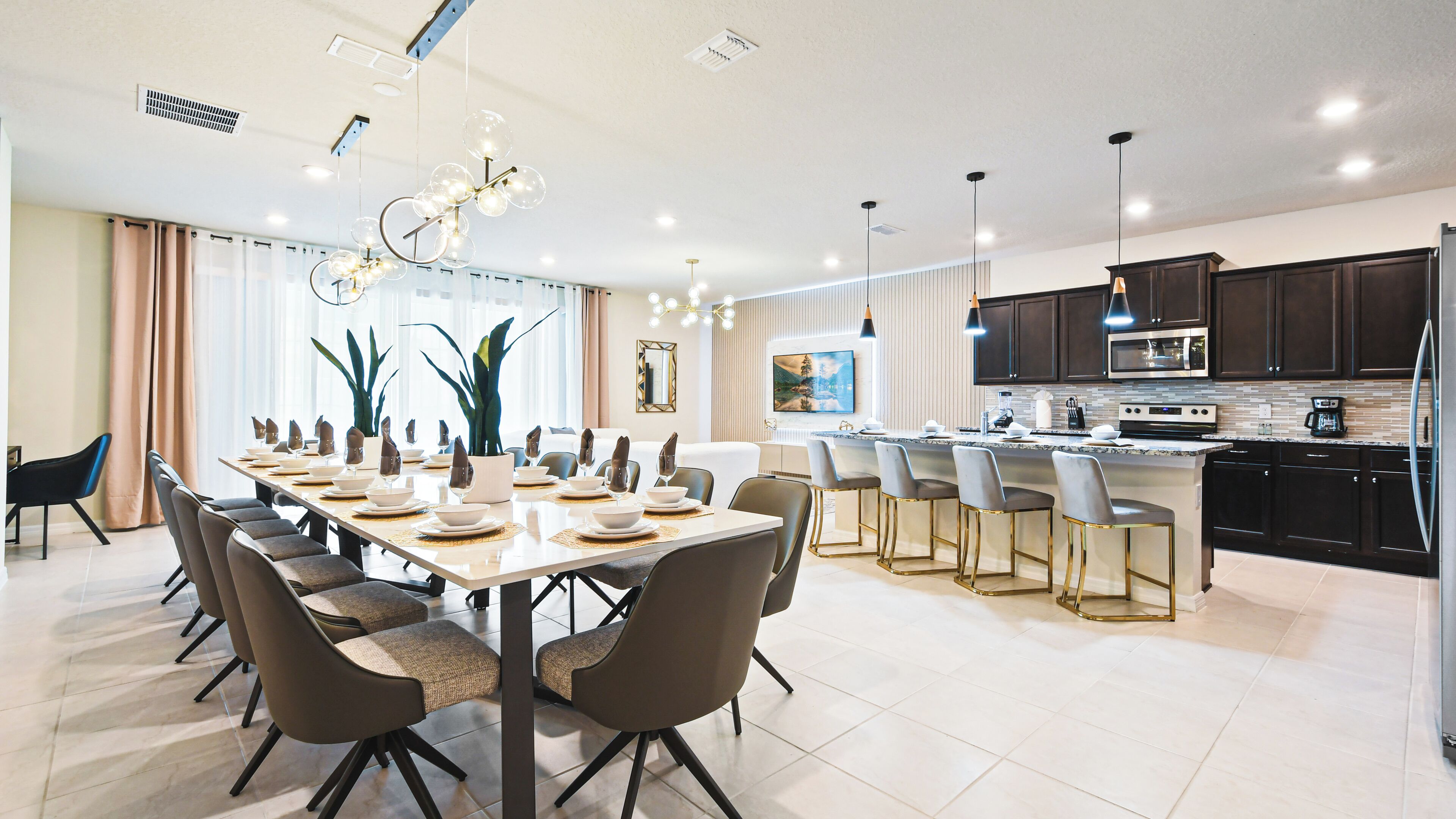 A modern kitchen with dark cabinets, a central island, and a dining area with a long table and chairs.
