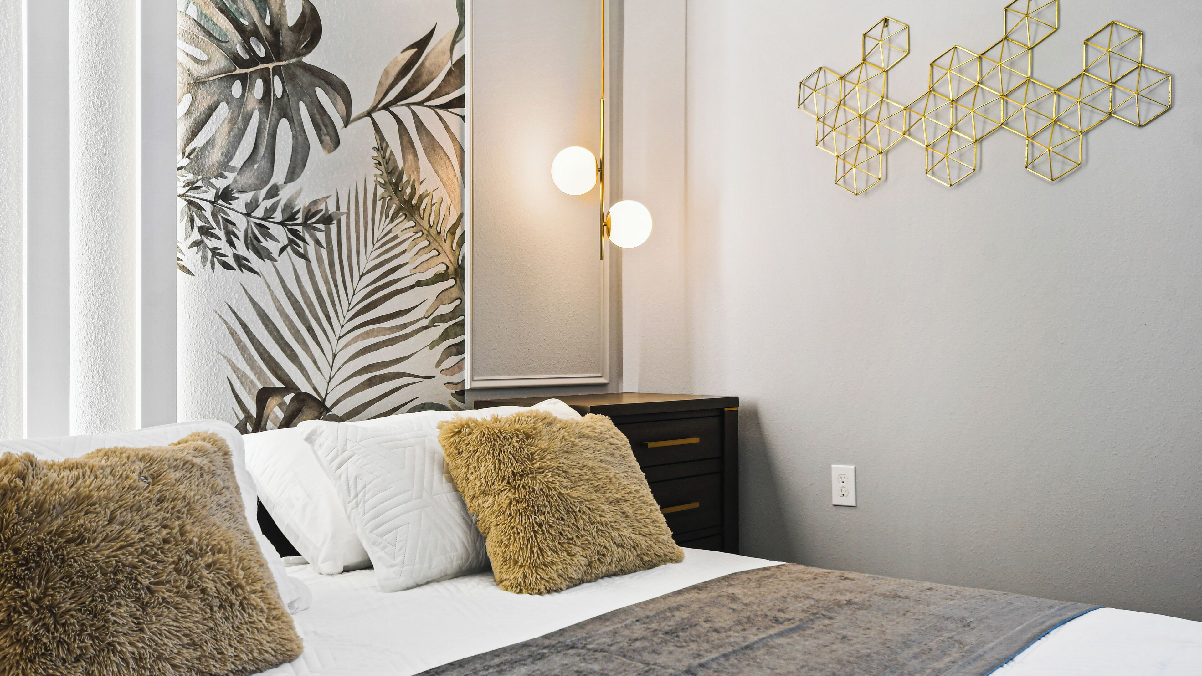 A bedroom with a bed, a dresser, a mirror, and a wall with geometric wall art.