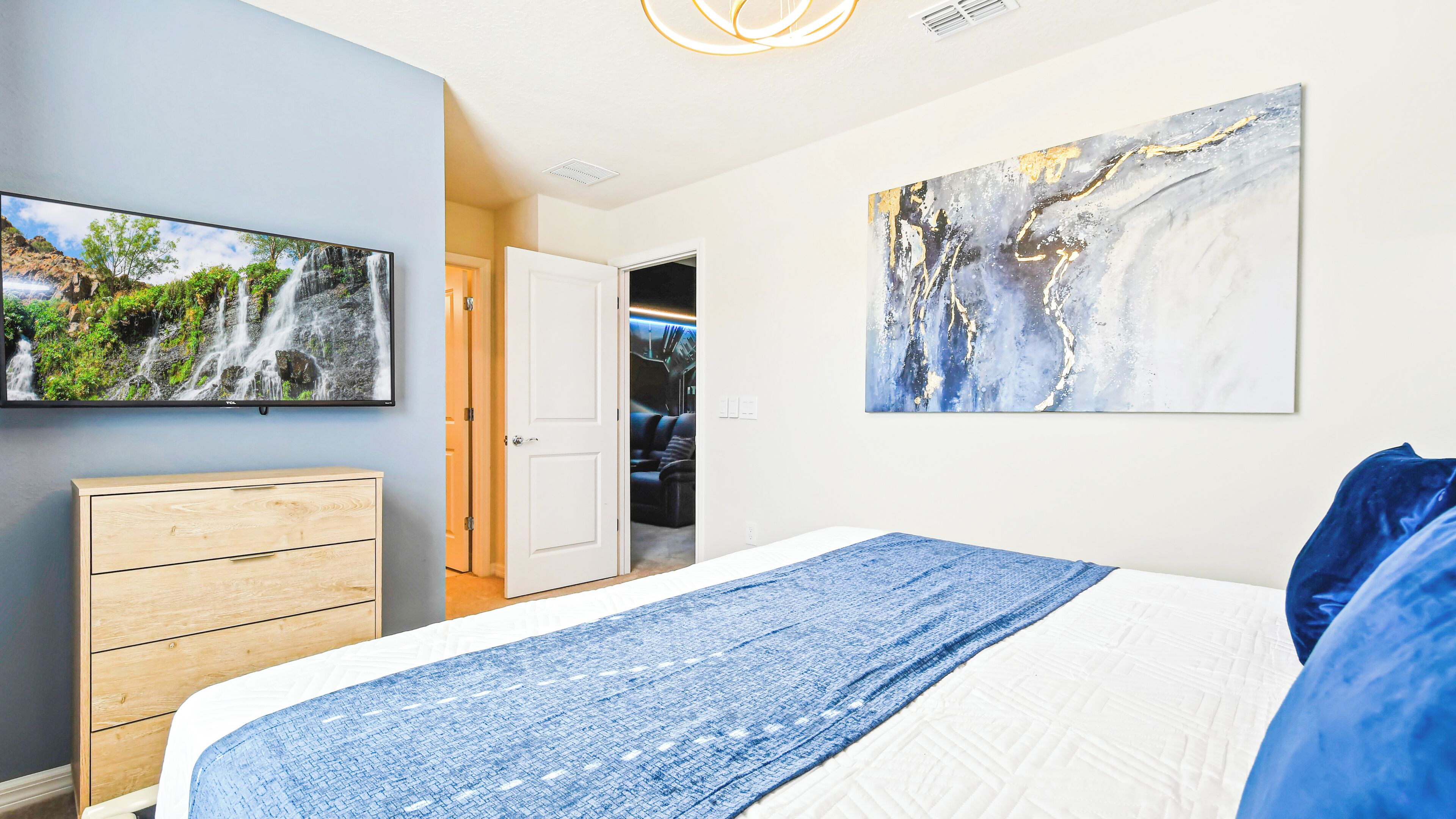 Une chambre à coucher avec un lit, un téléviseur fixé au mur, une porte donnant sur une salle de bain et un tableau.