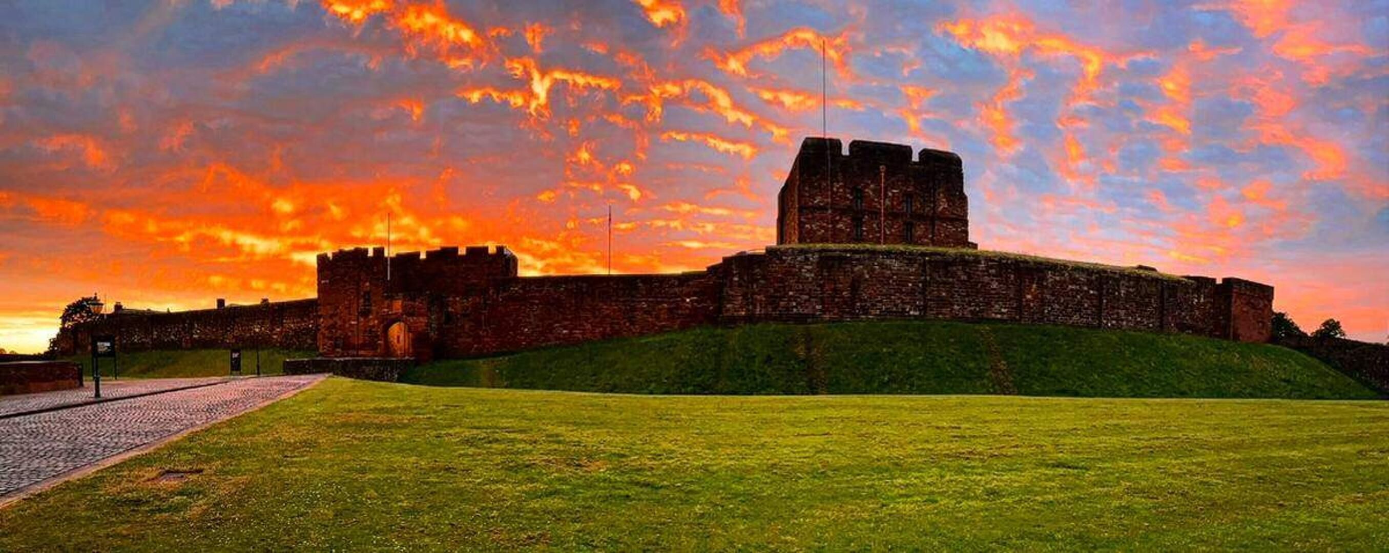 A historic castle with a large central tower, surrounded by a grassy area and a cobblestone path.