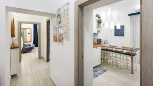 A modern kitchen with a dining area, a wooden floor, and a view into the adjacent living room.