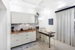 Une cuisine compacte avec des meubles blancs, un plan de travail en bois, un micro-ondes encastré et un coin repas comprenant une table et des chaises.
