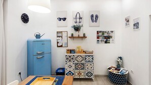 A room with a blue cabinet, a wooden table, a clock, and various wall decorations including framed pictures and a bulletin board.