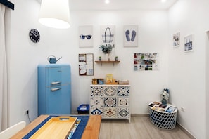 A room with a blue cabinet, a wooden table, a clock, and various wall decorations including framed pictures and a bulletin board.