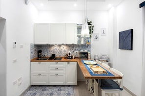 Une cuisine compacte avec des meubles blancs, un crédence carrelée bleue et blanche, un plan de travail en bois et un coin repas comprenant une table et des chaises.